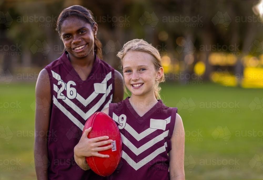 Image of two school-aged girls in football jerseys holding aussie rules ...