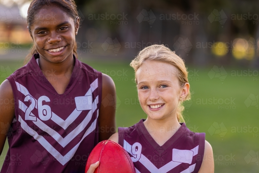 two schoolgirls in football uniform with the smallest holding a football - Australian Stock Image