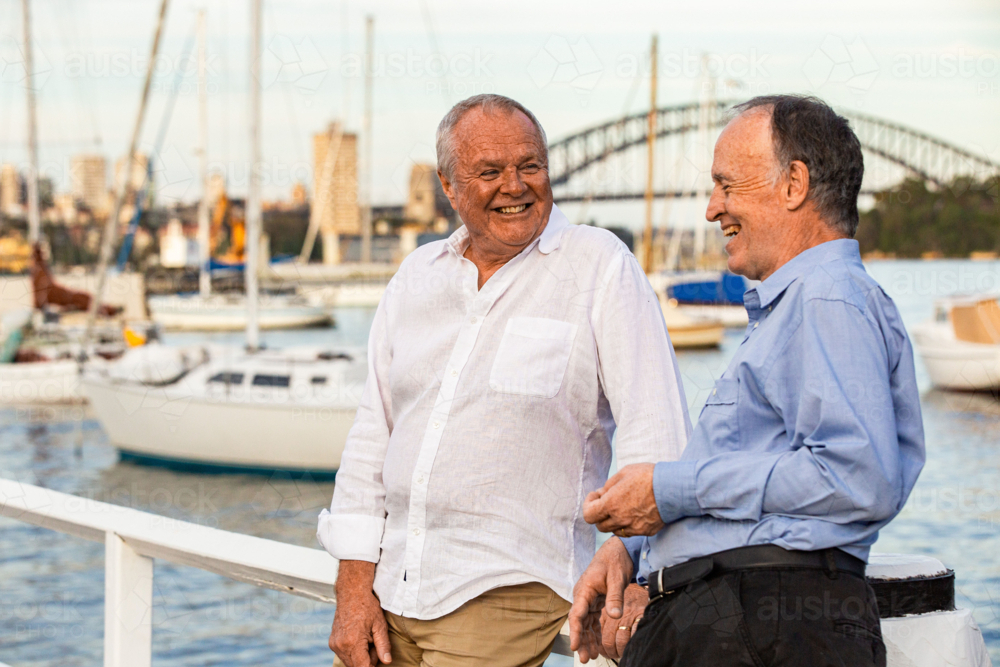 Two senior men standing and leaning against the wooden rails at the pier - Australian Stock Image