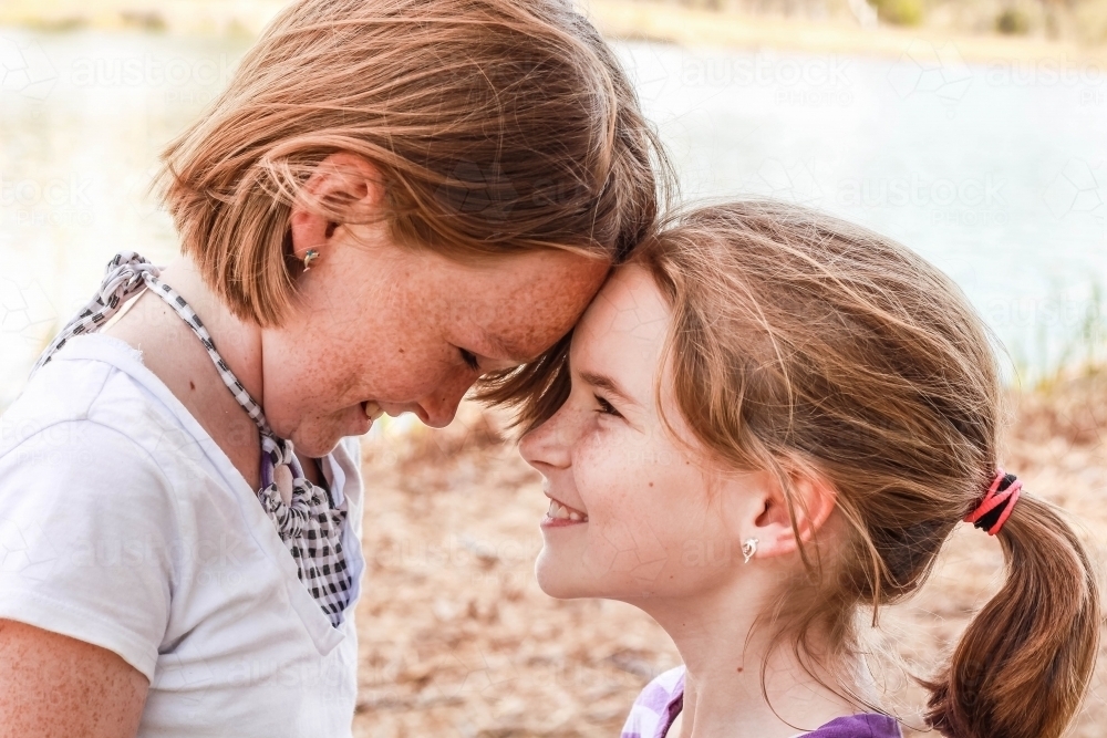 Two sisters with foreheads together looking at each other and smiling - Australian Stock Image