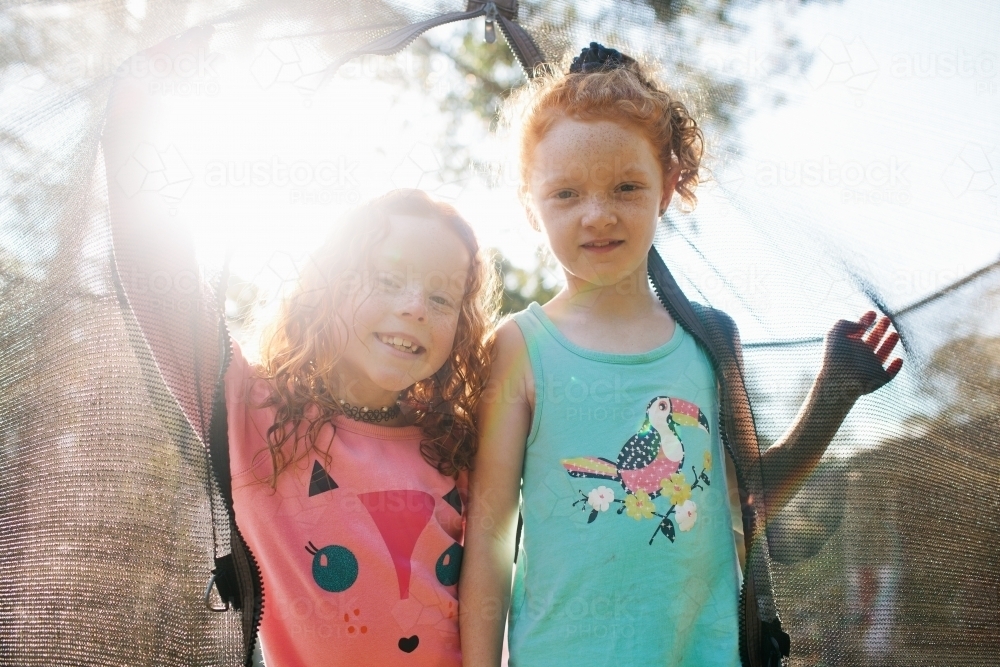 Two smiling girls looking through the net of a trampoline - Australian Stock Image