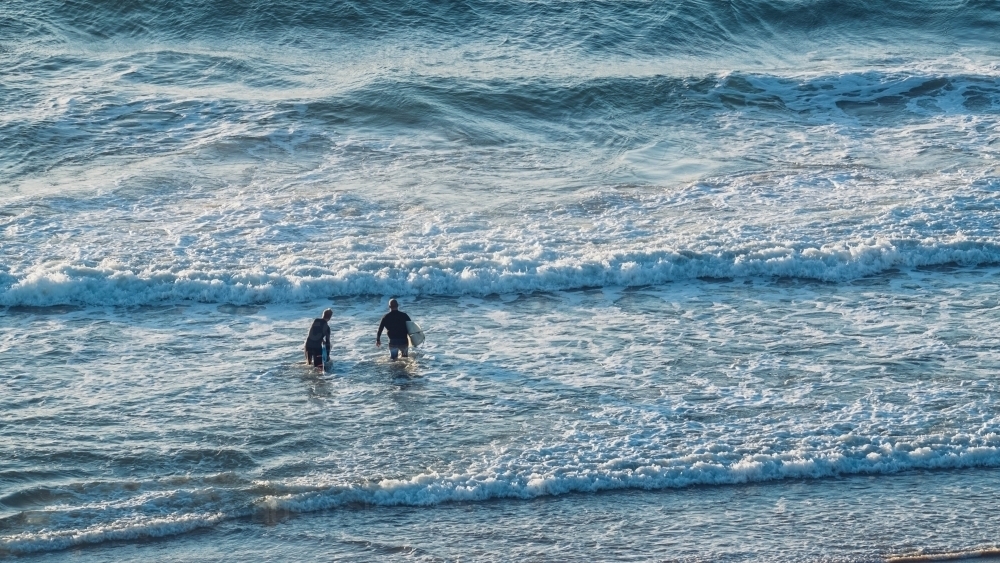 Two surfers with boards entering the surf - Australian Stock Image