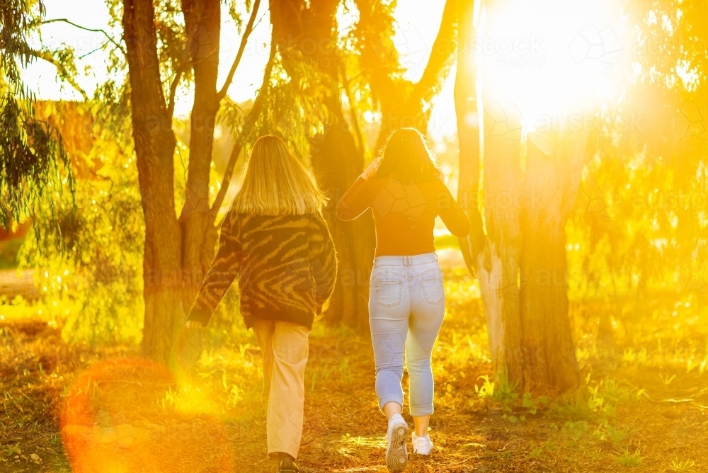 two teen girls walking away into golden light and sun flare - Australian Stock Image