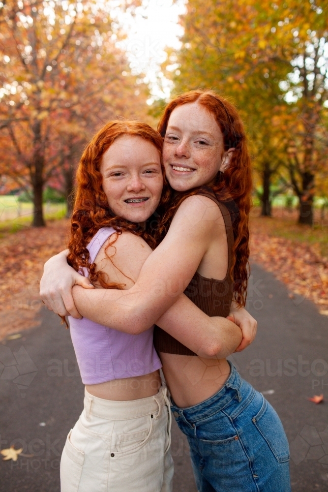 Two teenage girls standing in a street lined with Autumn trees - Australian Stock Image