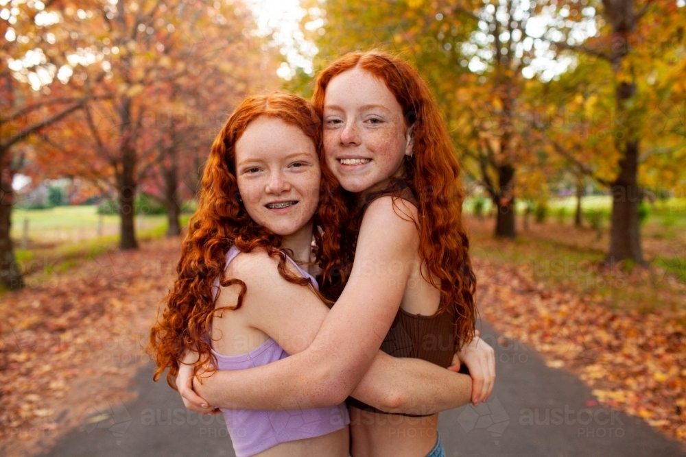 Two teenage girls standing in a street lined with Autumn trees - Australian Stock Image