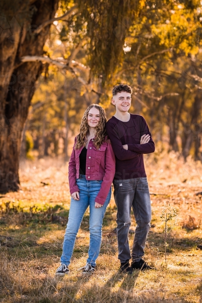 Two teens standing leaning on each other smiling - Australian Stock Image