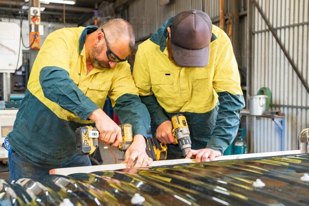 Two tradesmen cooperating to attach corrugated screening to an awning - Australian Stock Image