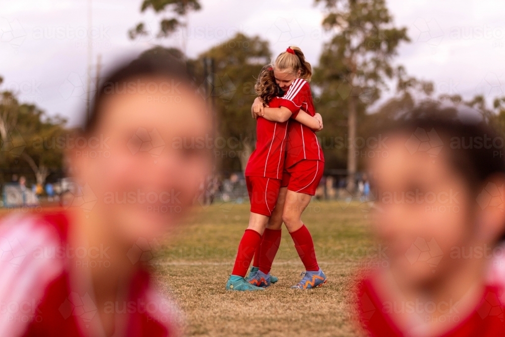 Two tween girls in a football team hug to celebrate a win - Australian Stock Image