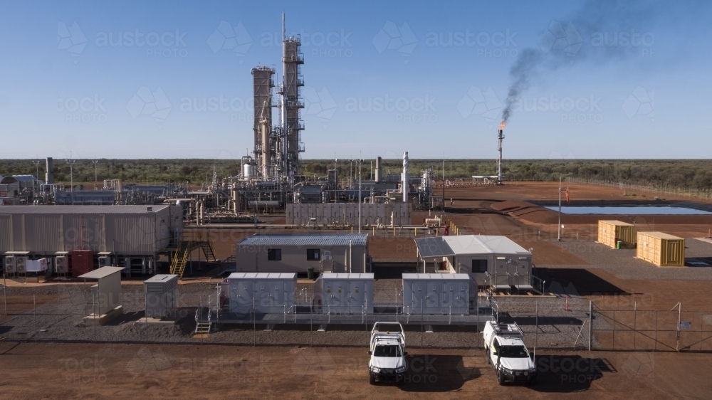 Two white work cars parked outside a power plant with a smoking flue-gas stack - Australian Stock Image