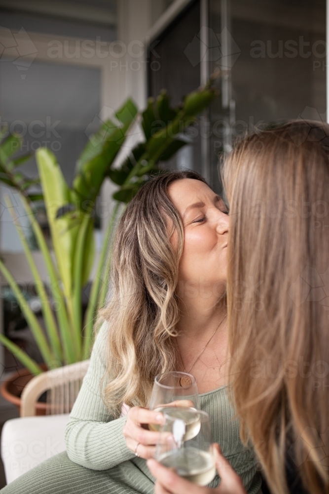 Two women kissing outside while holding glasses of wine - Australian Stock Image