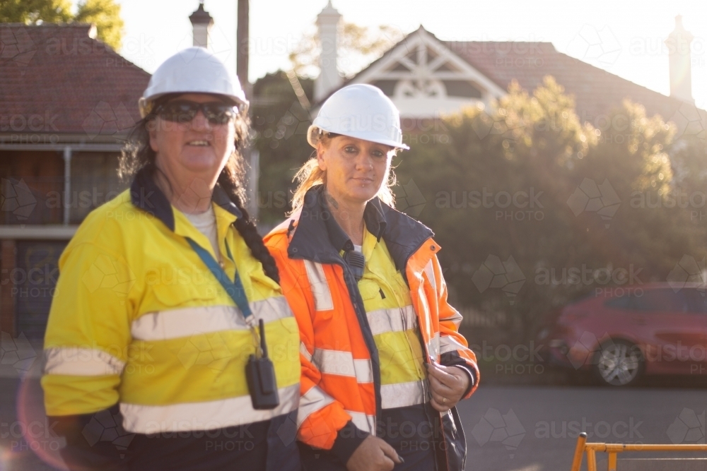 Two women road workers wearing white helmet with high vis in afternoon light - Australian Stock Image