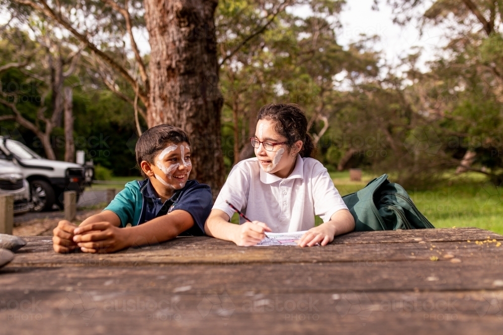 Two young Aboriginal children sitting at a table outdoors smiling - Australian Stock Image