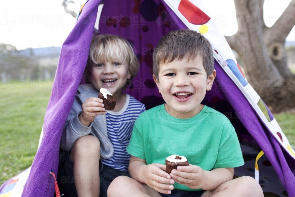 Two young boys eating cupcakes in a tent smiling - Australian Stock Image