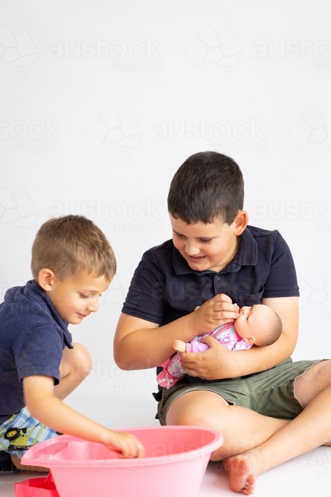 two young boys playing with a baby doll and baby bath - Australian Stock Image