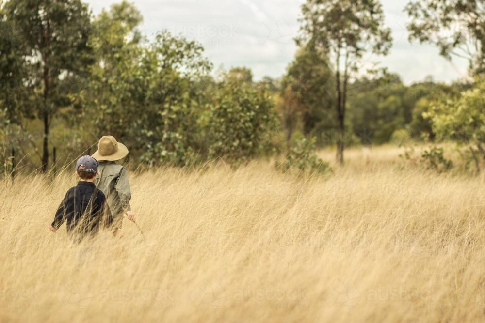 Two young boys walking through long grass in the paddock - Australian Stock Image