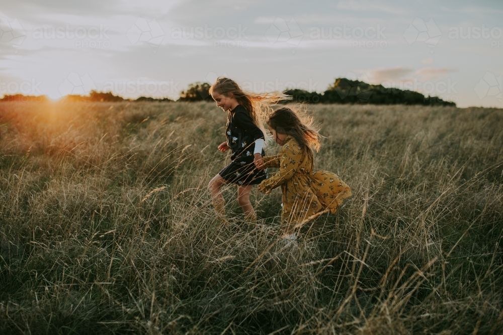 Two young fashionable children playing in long grass at sunset - Australian Stock Image