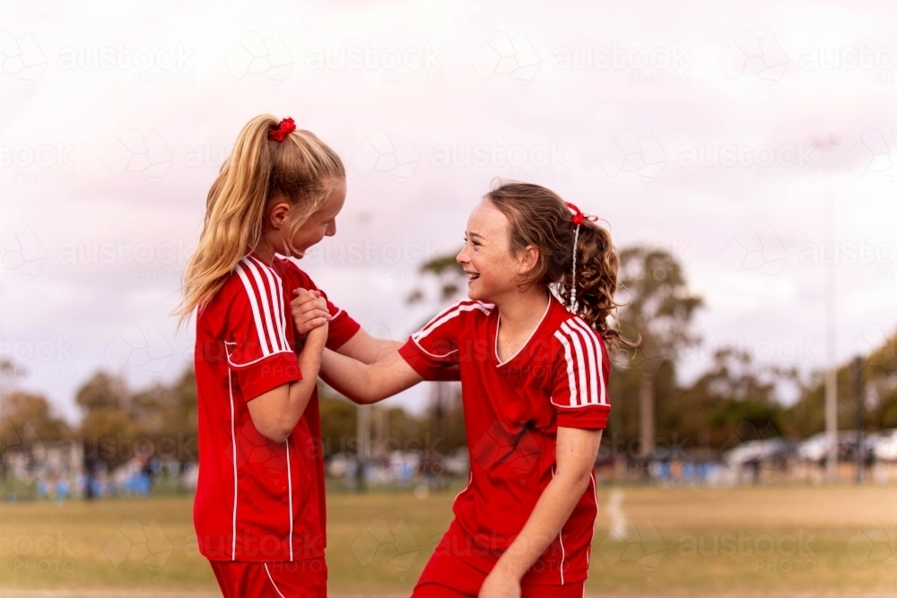 Two young female football players encouraging one another and smiling - Australian Stock Image