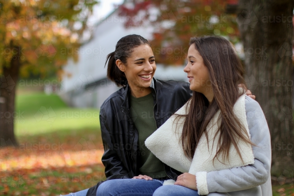 Two young female friends sitting together in an outdoor setting - Australian Stock Image