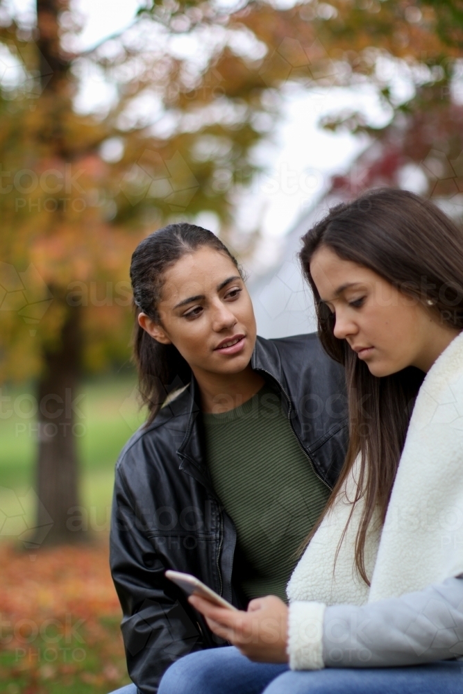 Two young female friends sitting together in an outdoor setting - Australian Stock Image