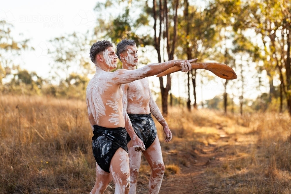 Two young First Nations men in traditional ochre paint telling stories and pointing with stick - Australian Stock Image