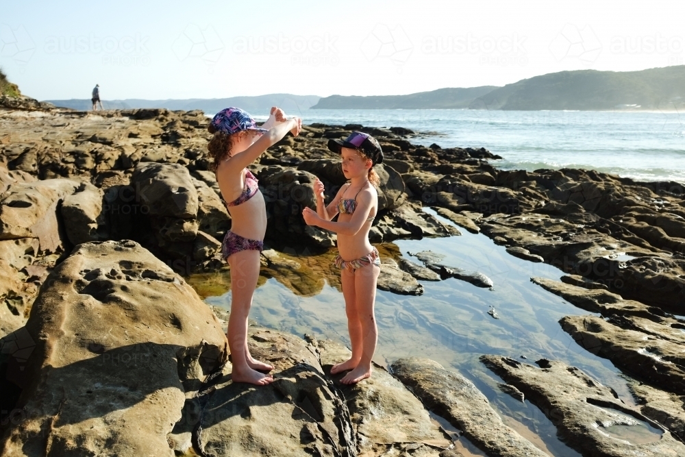 Two young girls playing on a rock platform at the beach - Australian Stock Image