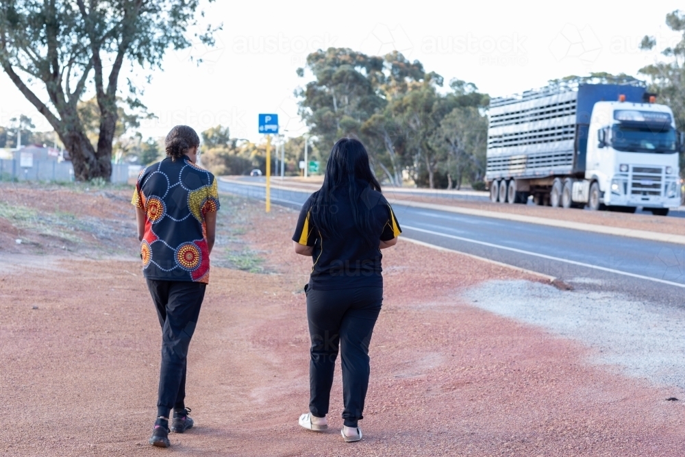 two young people walking near highway with truck on road - Australian Stock Image