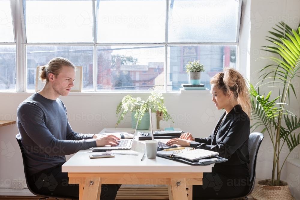 Two young people working at a shared desk horizontal - Australian Stock Image