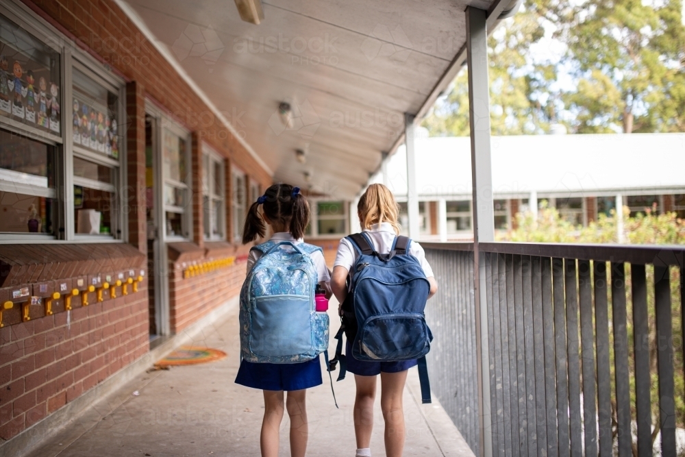 Image of Two young schoolgirls walking along outdoor school hallway ...