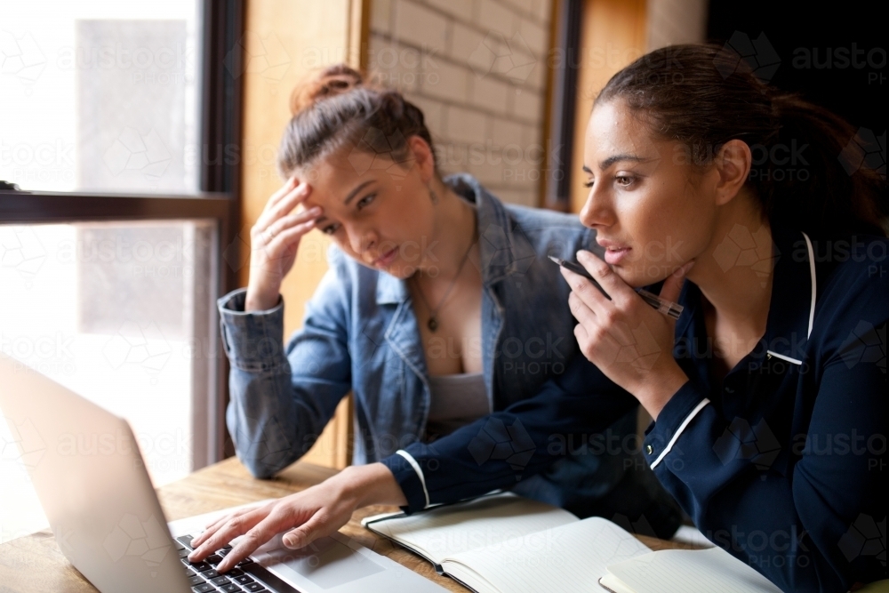 Two young women sitting at a desk in a classroom - Australian Stock Image