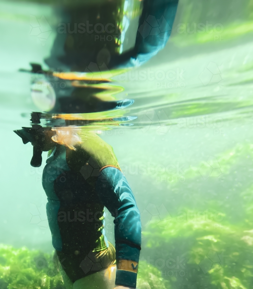 Underwater of woman’s upper torso wearing wetsuit top and snorkelling with reflection on surface - Australian Stock Image