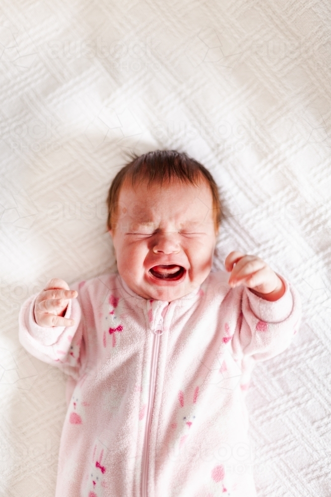 Unhappy baby on white crying reaching arms out - Australian Stock Image