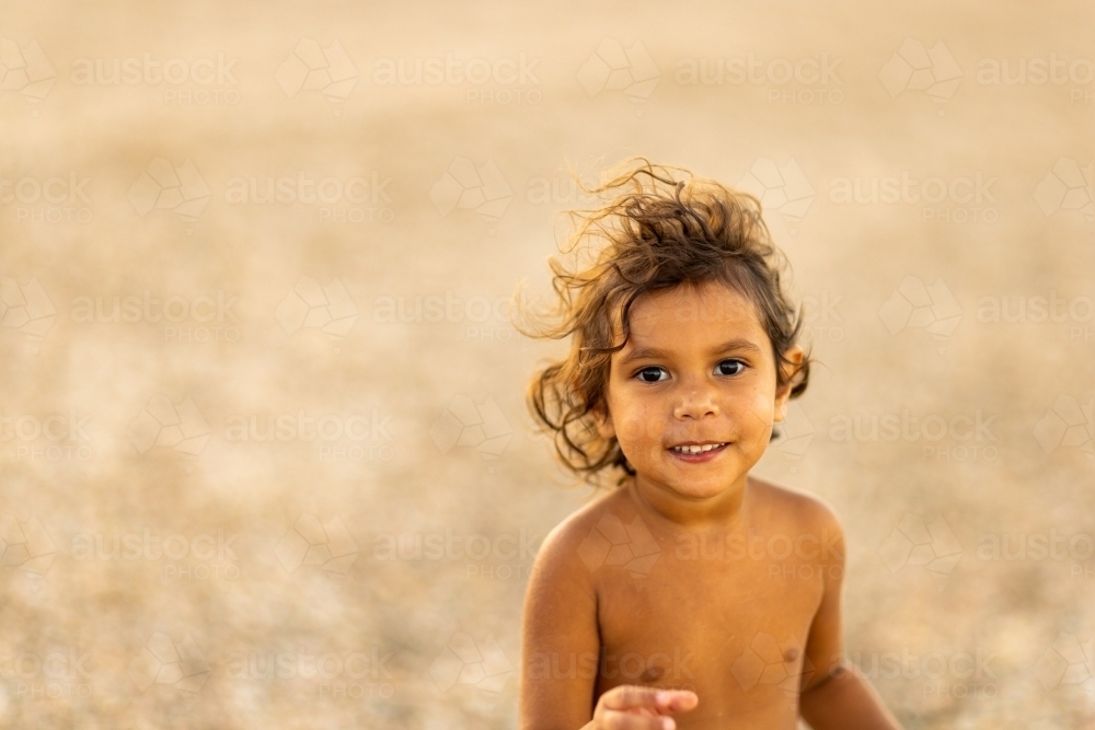 upper body of happy little aboriginal girl in soft light on beach - Australian Stock Image