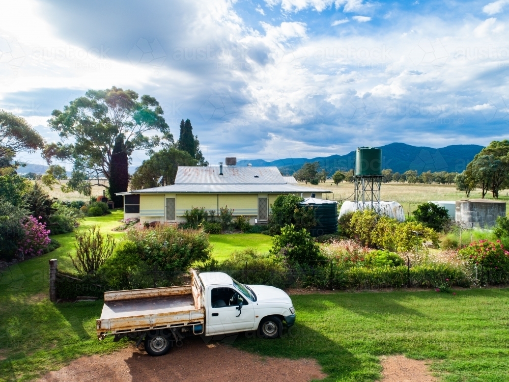 Ute parked outside of farmhouse on rural country property in morning light seen from aerial view - Australian Stock Image