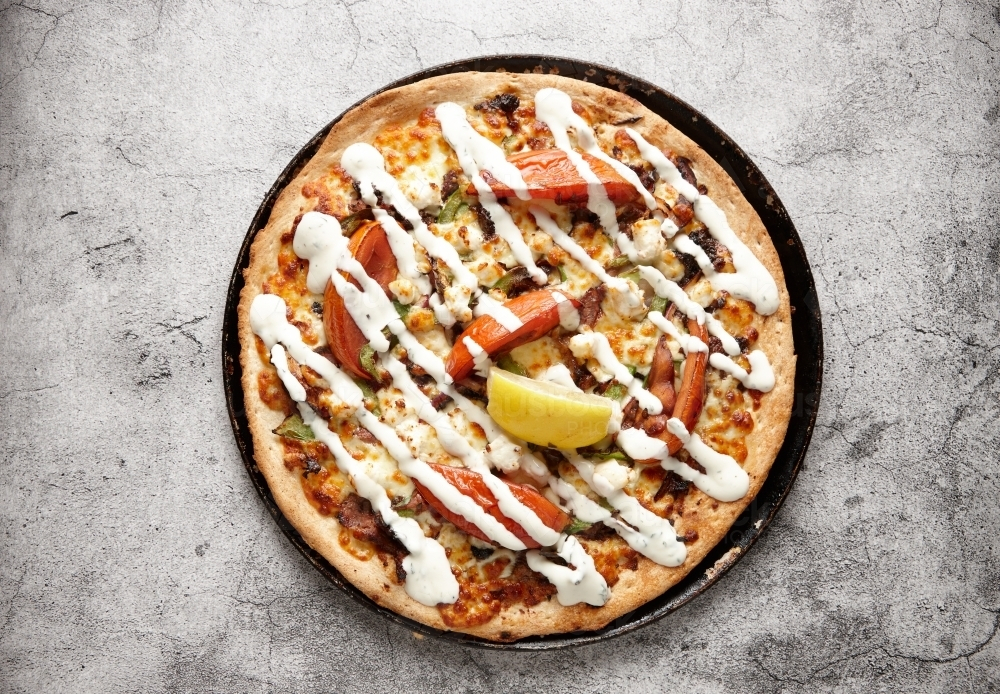 Vegetarian supreme pizza drizzled with white sauce and topped with a lemon slice - Australian Stock Image