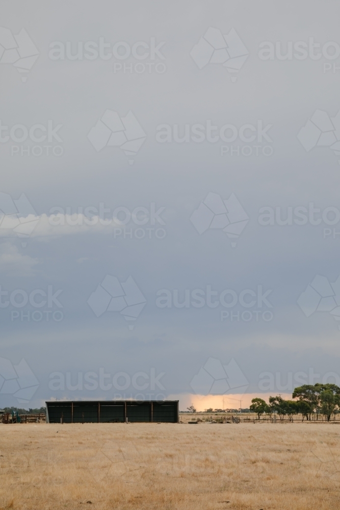 Vertical image of hay shed on farm with storm in the distance - Australian Stock Image