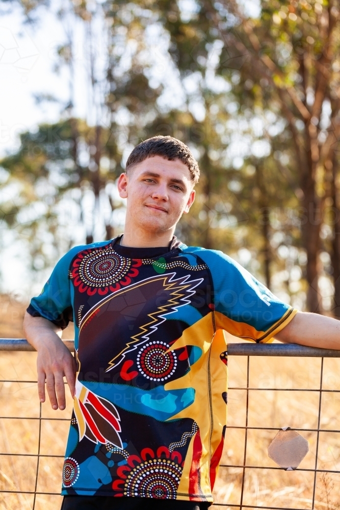 Vertical portrait of teenage Aboriginal boy leaning on gate - Australian Stock Image