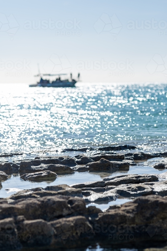 Vertical shot of a boat offshore of Heron island with rocky foreground - Australian Stock Image