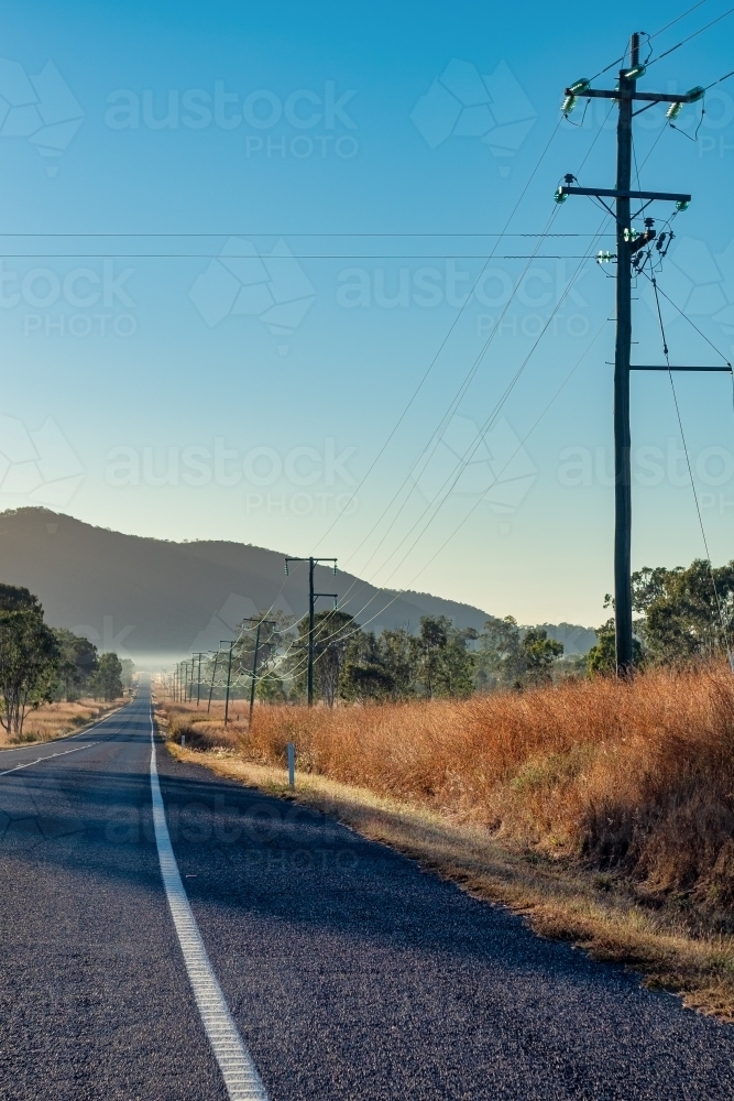 Vertical shot of a road towards Mount Morgan with power poles and lines beside - Australian Stock Image