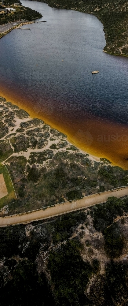 vertical shot of an island with boat floating, bushes, road, and yellow sand on a sunny day - Australian Stock Image