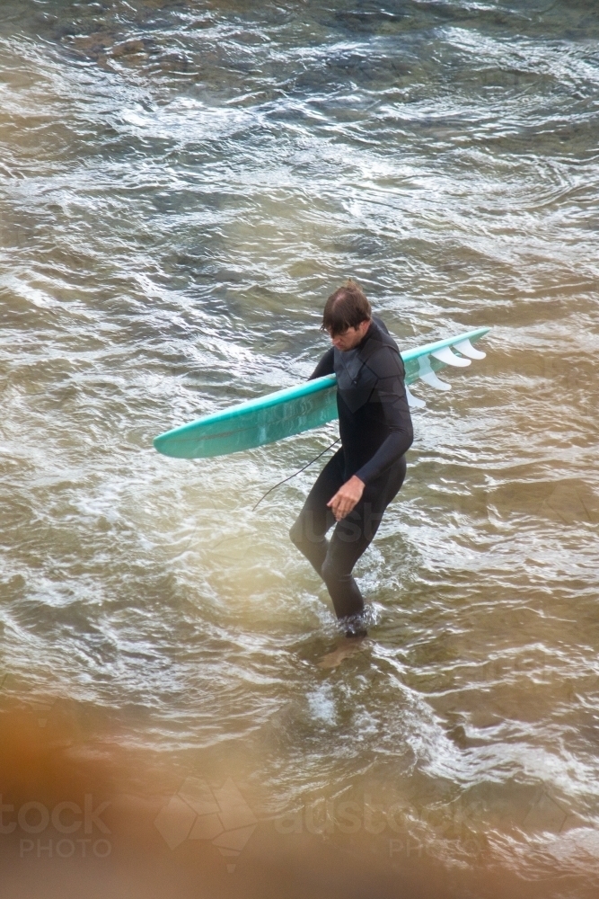 Vertical shot of man wearing wetsuit and carry surfboard walking out of the ocean after a session - Australian Stock Image