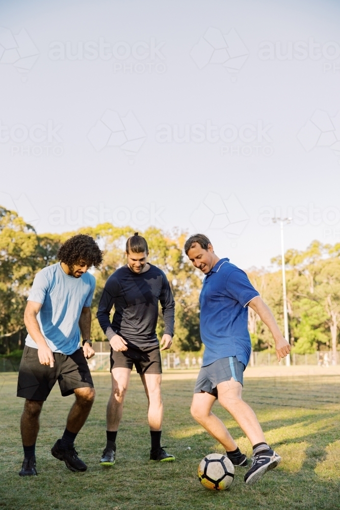 vertical shot of men playing soccer in the field on a sunny day with clear skies - Australian Stock Image