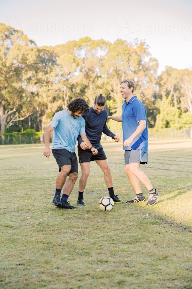 vertical shot of men playing soccer in the field on a sunny day with clear skies - Australian Stock Image