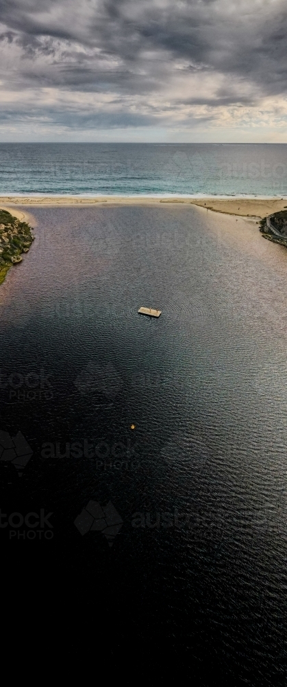 vertical shot of the ocean water with a floating wooden raft under cloudy skies - Australian Stock Image