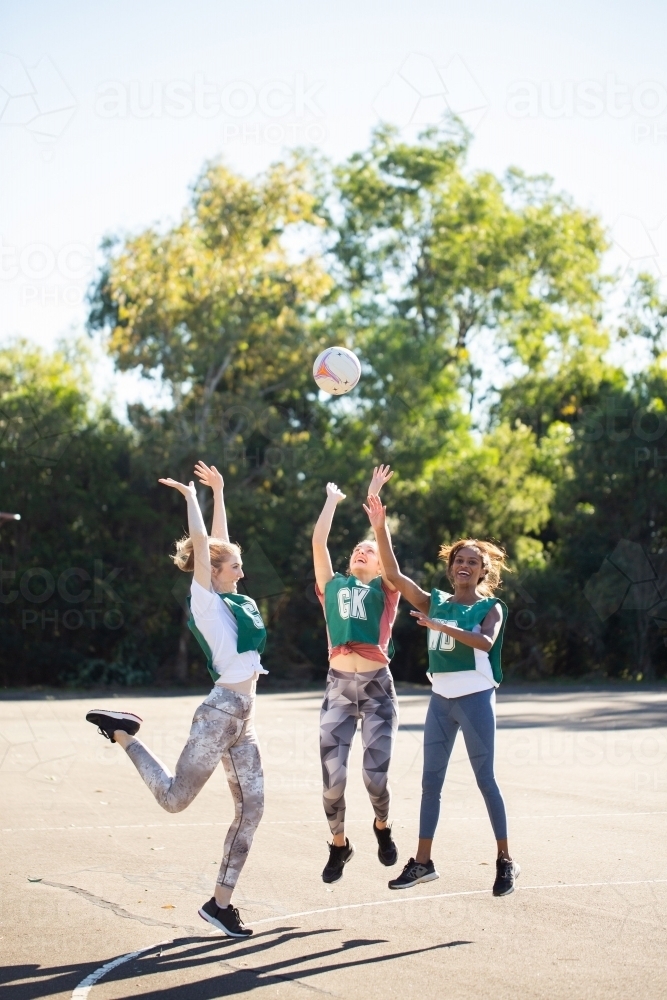 vertical shot of three women jumping in mid air trying to catch a ball on a sunny day - Australian Stock Image