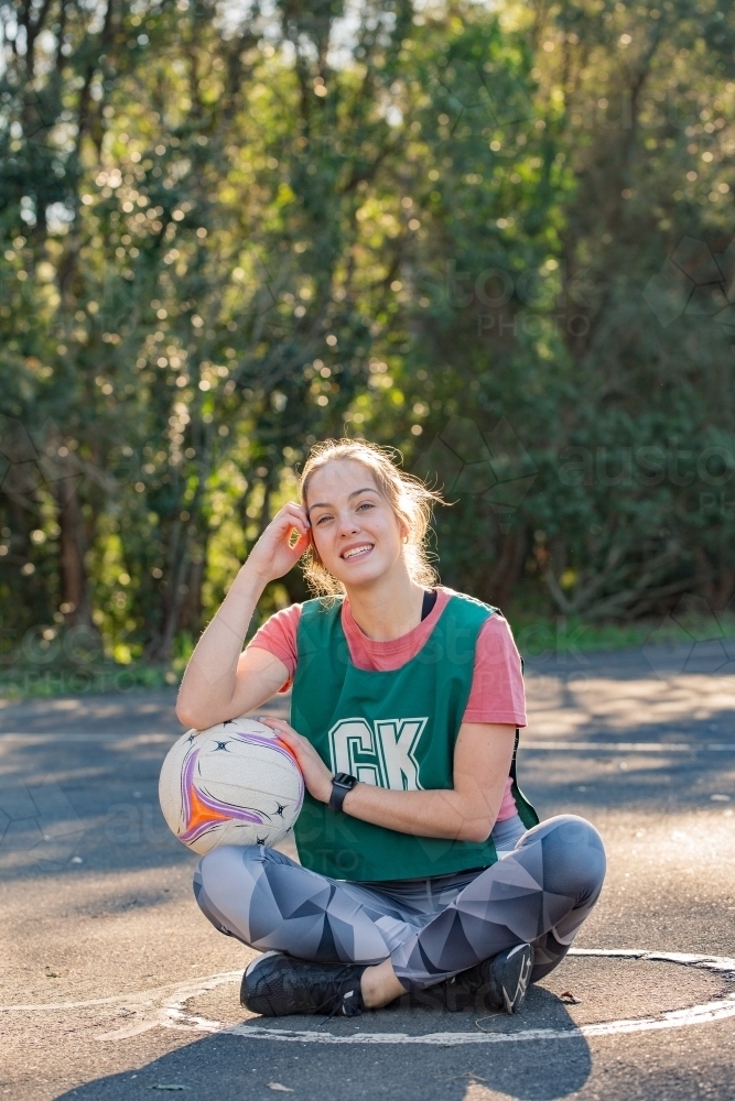 vertical shot of young sporty woman sitting on the ground while touching the ball and her face - Australian Stock Image