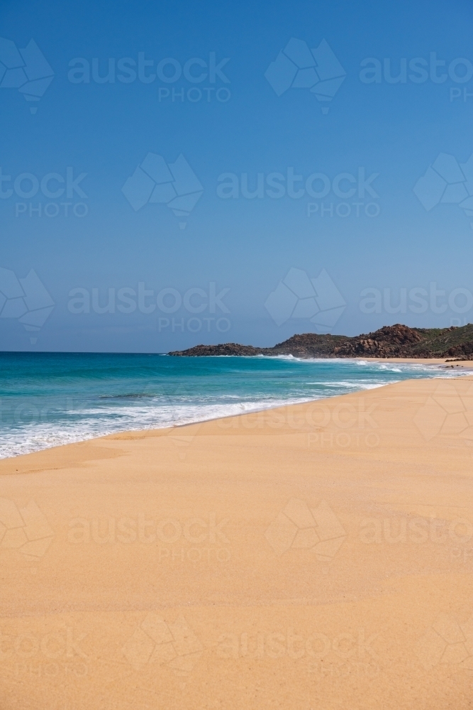 Vertical view looking along sandy beach with waves towards a headland - Australian Stock Image