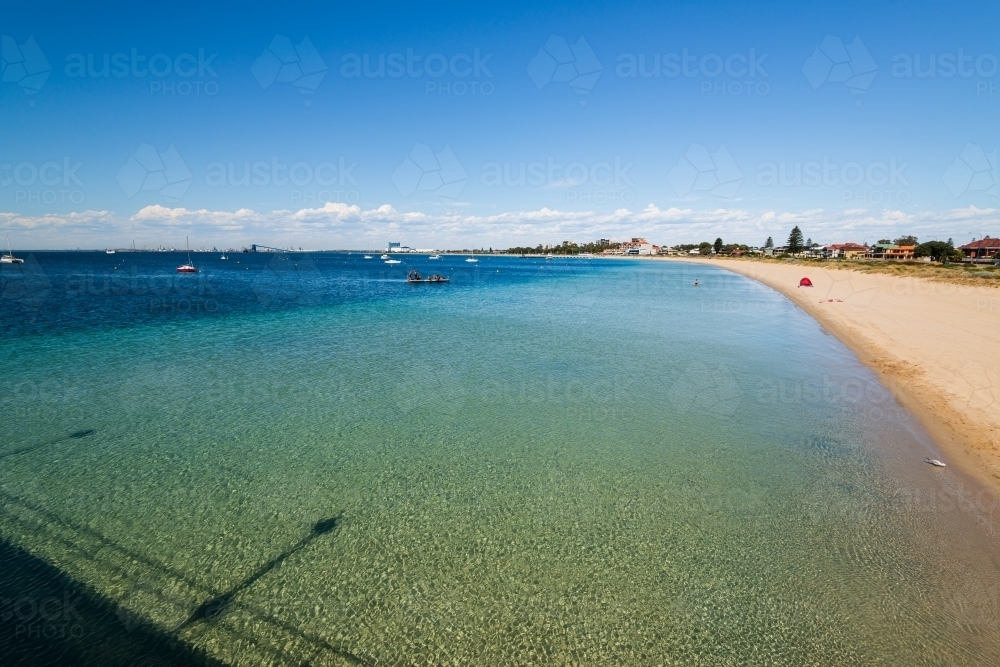 View from jetty of sandy beach, clear green blue water and swimming platform with people - Australian Stock Image