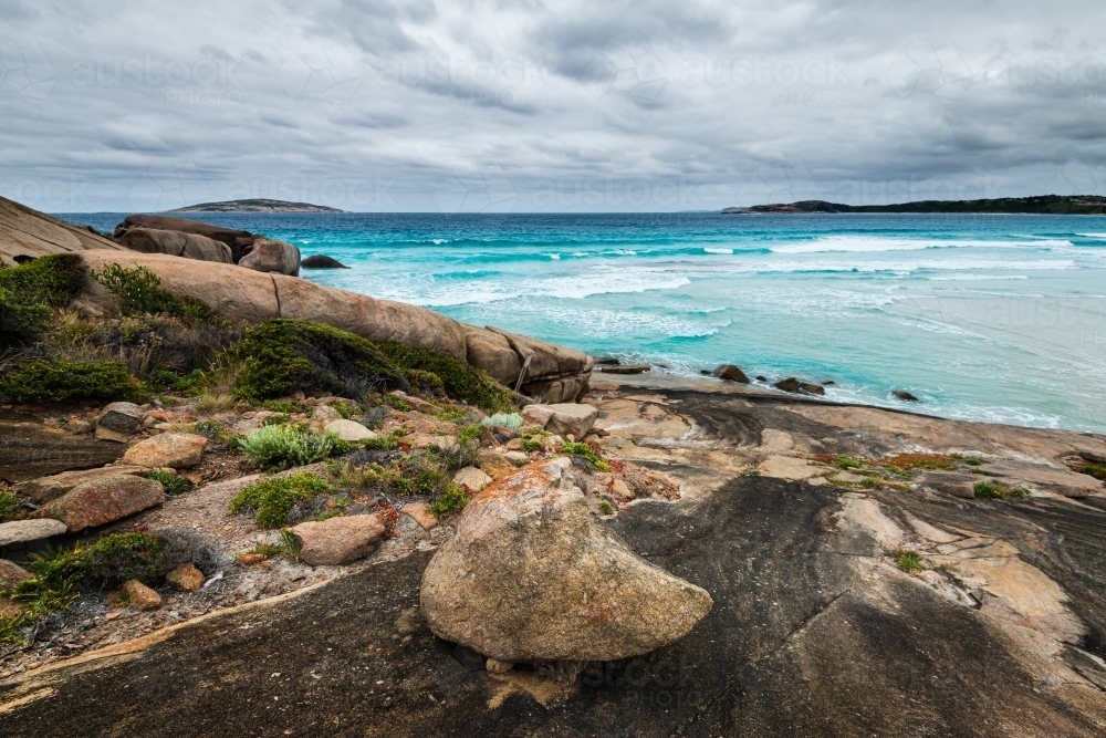 View of beach stormy sky Turquoise ocean with leading lines in colourful rocky foreground - Australian Stock Image