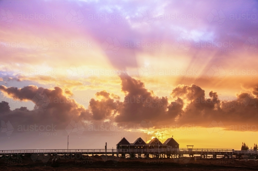 View of Busselton jetty silhouette with sun rays shining through clouds - Australian Stock Image