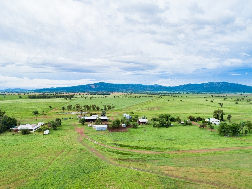 View of distant farm home area with house and sheds among green paddocks - Australian Stock Image